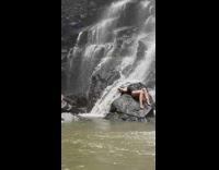 Woman in swimsuit posing on rock in front of small waterfall