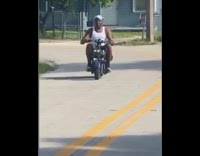 Guy rides small blue motorcycle neighborhood street