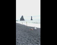 Lady walks along black sand beach shore 