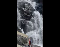 Couple Takes Photos Next to Big Waterfall 