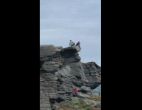 Person climbs grey rock cliff guy poses 