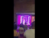 Pole dancer performs in store window with audience outside 