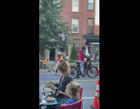 Guy balances trash can on head on bike