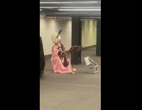 Lady wearing pink dress plays cello at subway station
