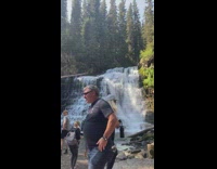 Man in a cowboy hat sits on the tree near the waterfalls