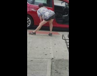 Woman stands next to red car on sidewalk and sticks out her butt to stretch