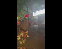 Two guys ride dirt bike together one guy sits on chair 