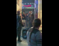 Shirtless guy in demon mask does bicep curls in front of H&M, guy dances behind him