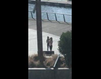 Two girls take selfies outside by water 