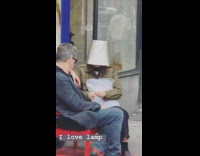 Person sits on outdoor bench with lampshade on head