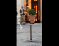 Person baggy pants poses beside store bushes