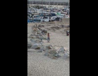 Girl grey leggings walk beach boats boulders