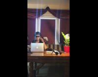 Guy in suspender black vest and sunglasses dance to song on laptop at dinner table