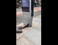 Guy laying down on sidewalk with earbuds plugged into a digital panel