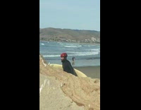 guy wearing red helmet walking on beach with surfboard 