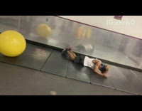 Guy tries to sit and bounce on yellow medicine ball and falls on pads at the gym