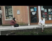 Man white outfit sits near the river in front of a store