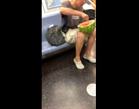 Woman in light blue crocs eats half watermelon with spoon on the subway train