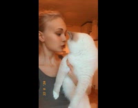 Grey shirt girl holds kisses white cat 