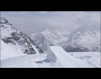 Skier jumps high off snow ramp and flails arms and legs in the air