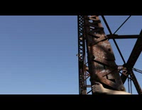 Shirtless guy jumps off brown bridge into river 