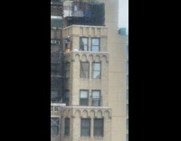 Construction worker standing on yellow barrel on buildings ledge
