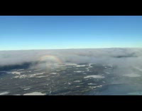 Airplane flies through low white cloud rainbow 