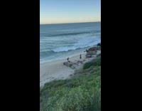 Woman in black dress with a photographer behind at the beach