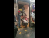 Guy walking his scooter off the subway train to exit 
