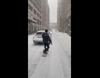 Grey car pulls guy on snowboard street