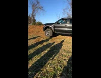 Black truck drives over grass hill 