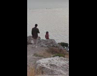 Woman crop top sits on cliff with boyfriend behind