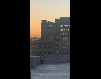 Red shoes guy squats rooftop ledge sunset