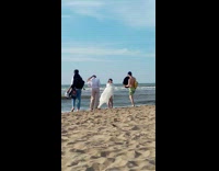 Woman covered in white blanket poses at the beach