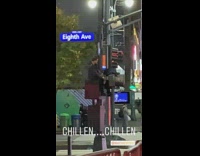 Guy with backpack chills out on top of stoplight post on eighth ave