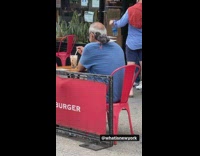 A man eating with a pigeon on his shoulder