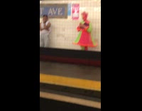 Woman in pink and bright green dress texts on her phone in subway station