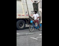 Collab WINY - Man balance trash can on head beside garbage truck