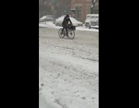 Guy rides bicycle through snow black bag