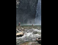 Shirtless guy walk towards large waterfalls rocks