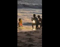 Woman pink top kneels and faces the beach