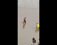Brown bodysuit girl kneels beach sand guy
