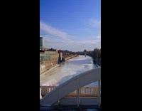 Drone flyover footage of a frozen river and a bridge and buildings 
