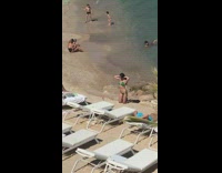 Green bikini girl kneels sand white chairs