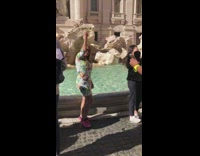 Woman in floral dress pretends to throw coin in fountain