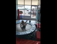 Little girl shoots basketball into hoop while on trampoline and falls back
