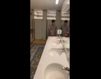 Guy makes beer pong shot in red solo cup across bathroom sinks