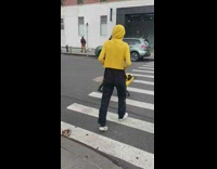 Woman in matching hoodie walks yellow robot dog across the street