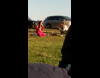 Girl red bralette pants kneels grass park 