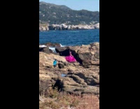 Woman pink dress poses at beach rocks